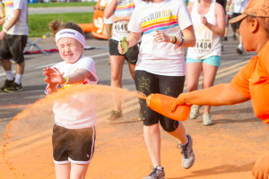 A young girl closes her eyes as she runs through a burst of orange color.