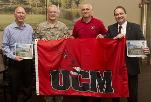 University of Central Missouri alumnus Patrick Stueve, second from left, presents one of two UCM flags with the Mule head logo to President Charles Ambrose, left. Ambrose had the flags sent to Stueve in Afghanistan.  Joining Stueve and Ambrose for the presentation were Jeff Huffman, third from left, director of Military and Veteran Services, and Tony Monetti, assistant dean of aviation and executive director of the Max B. Swisher Skyhaven Airport.