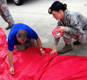 Senior Airman Jessica Lindblom assists a member of the Kansas City Royals events team in taping a tear in the 300-foot American flag moments before the 120-member group of military personnel from Whiteman Air Force Base presented the flag prior to the start of the game.